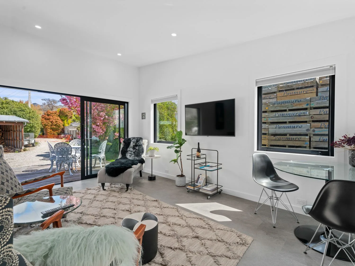 A bright living room with seating, a wall-mounted television, and glass doors opening onto a garden.