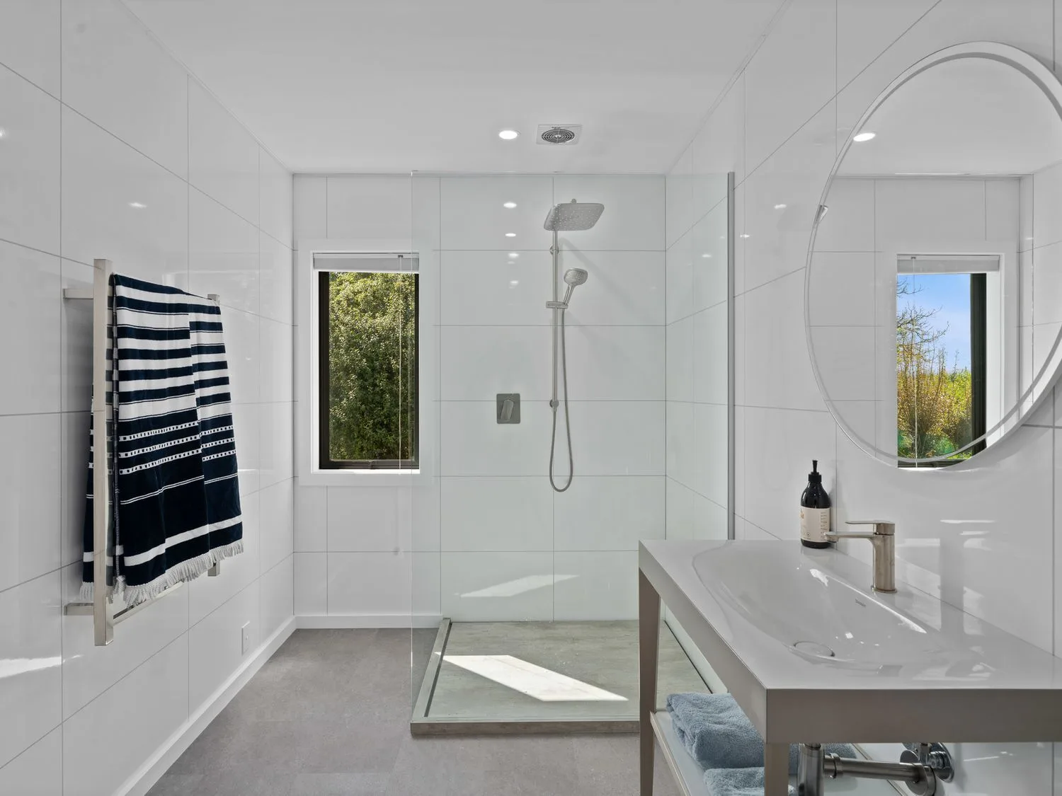 Un baño alicatado con ducha de cristal, lavabo con mueble, espejo redondo y ventana.