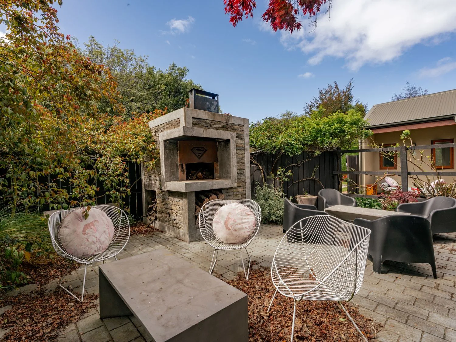 Un patio exterior con una chimenea de piedra y asientos de alambre.