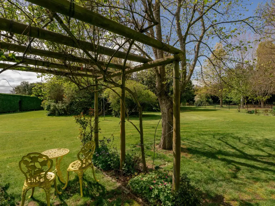 Un jardín con césped verde, árboles, una pérgola de madera y una mesa y sillas de metal amarillo en Caledonia - Earnscleugh Holiday Home, en Earnscleugh