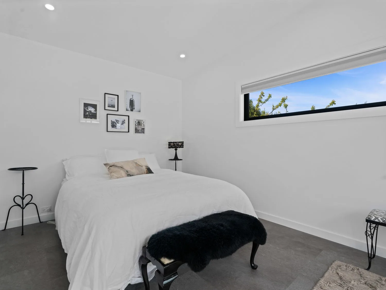 Un dormitorio con una cama blanca y una ventana horizontal larga con árboles visibles afuera.