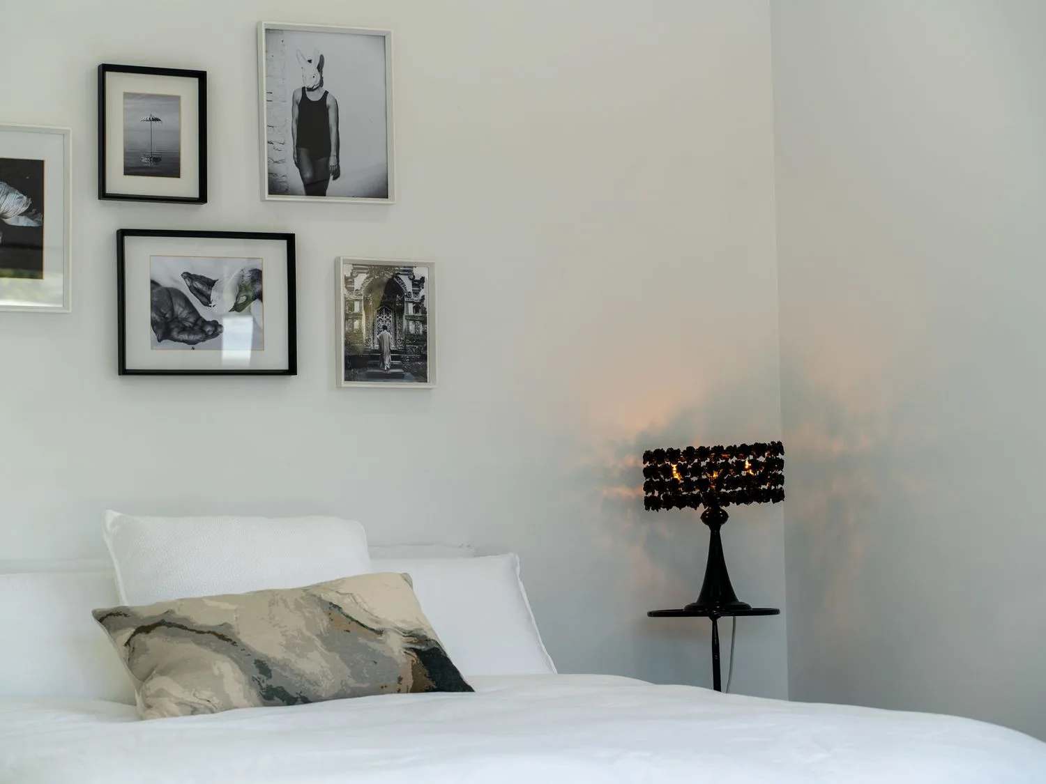Un dormitorio con una cama con ropa de cama y almohadas blancas, un cojín decorativo y cuadros enmarcados en blanco y negro en la pared junto a una lámpara de mesa negra en Caledonia - Earnscleugh Holiday Home, en Earnscleugh