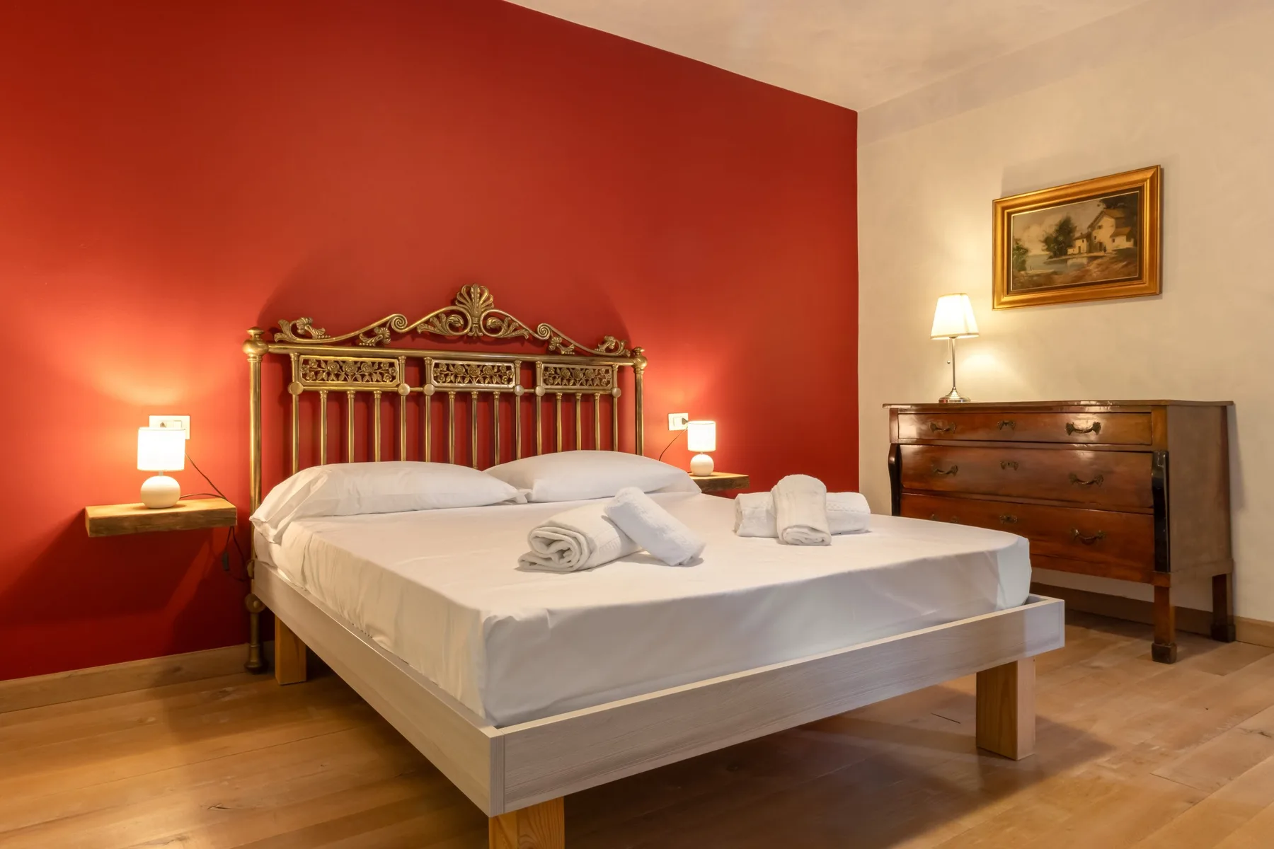 A bedroom with a bed against a red wall and a wooden dresser.