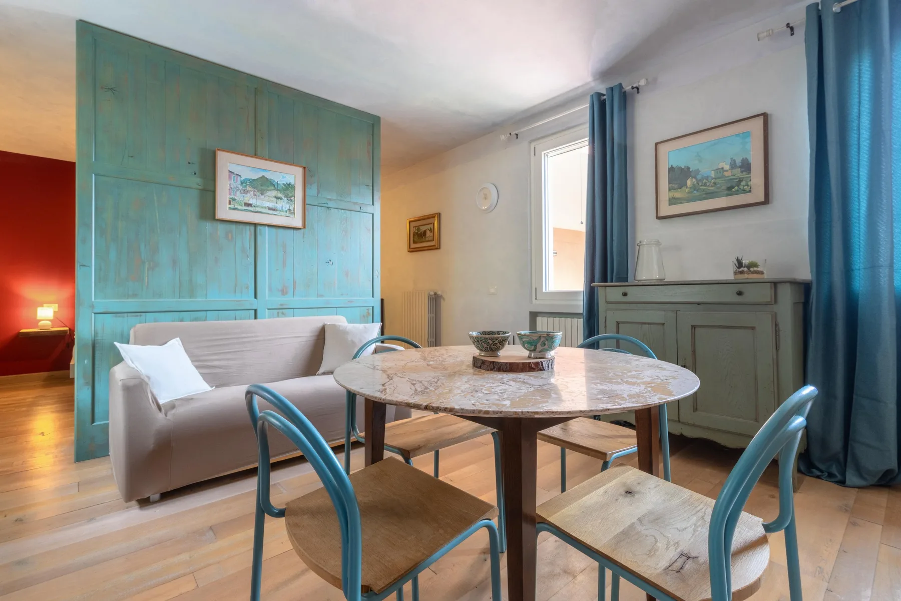 A dining area with a round table and chairs beside a sofa and blue curtains.