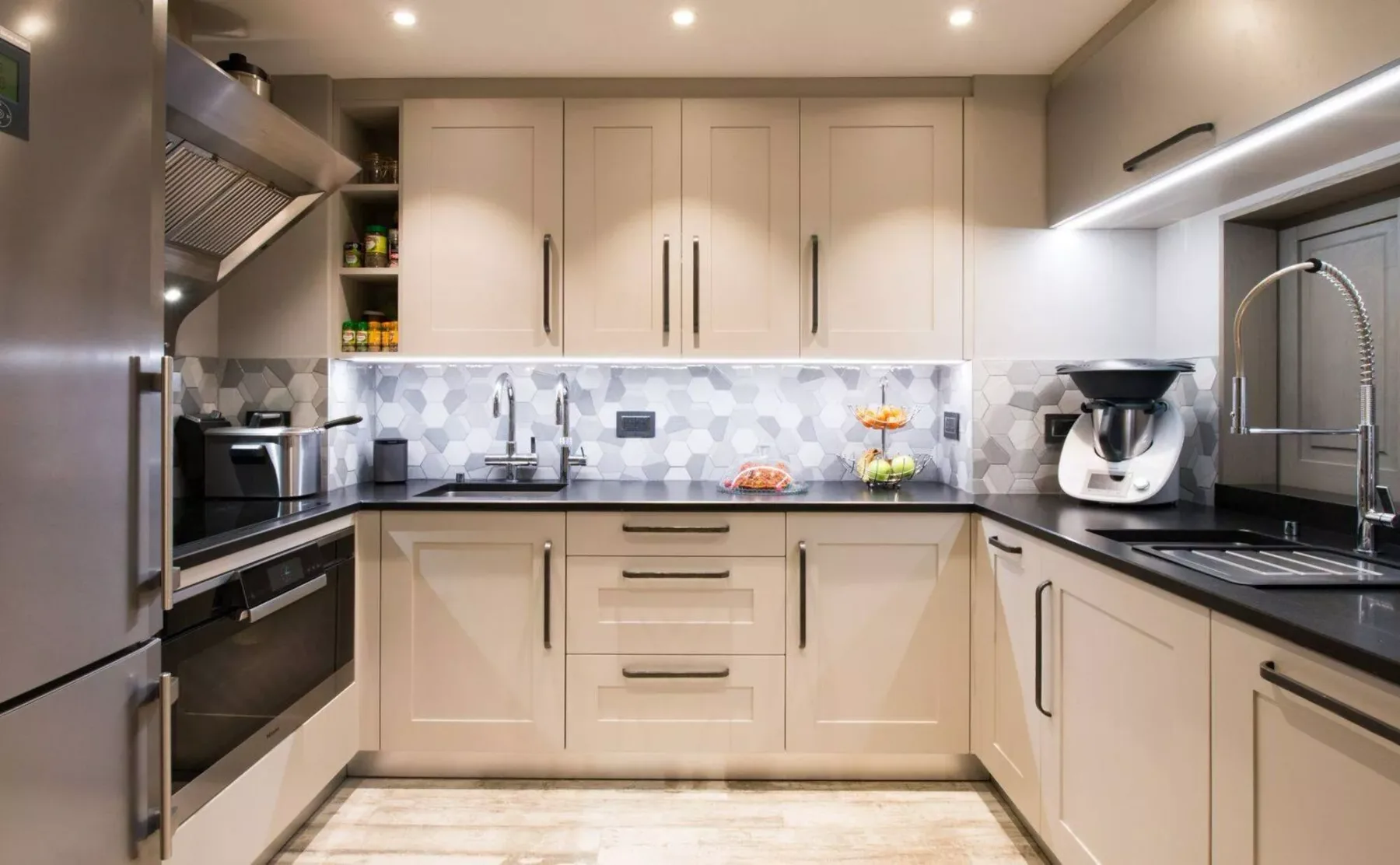 A modern kitchen with pale cabinets, dark countertops, and a tiled backsplash.