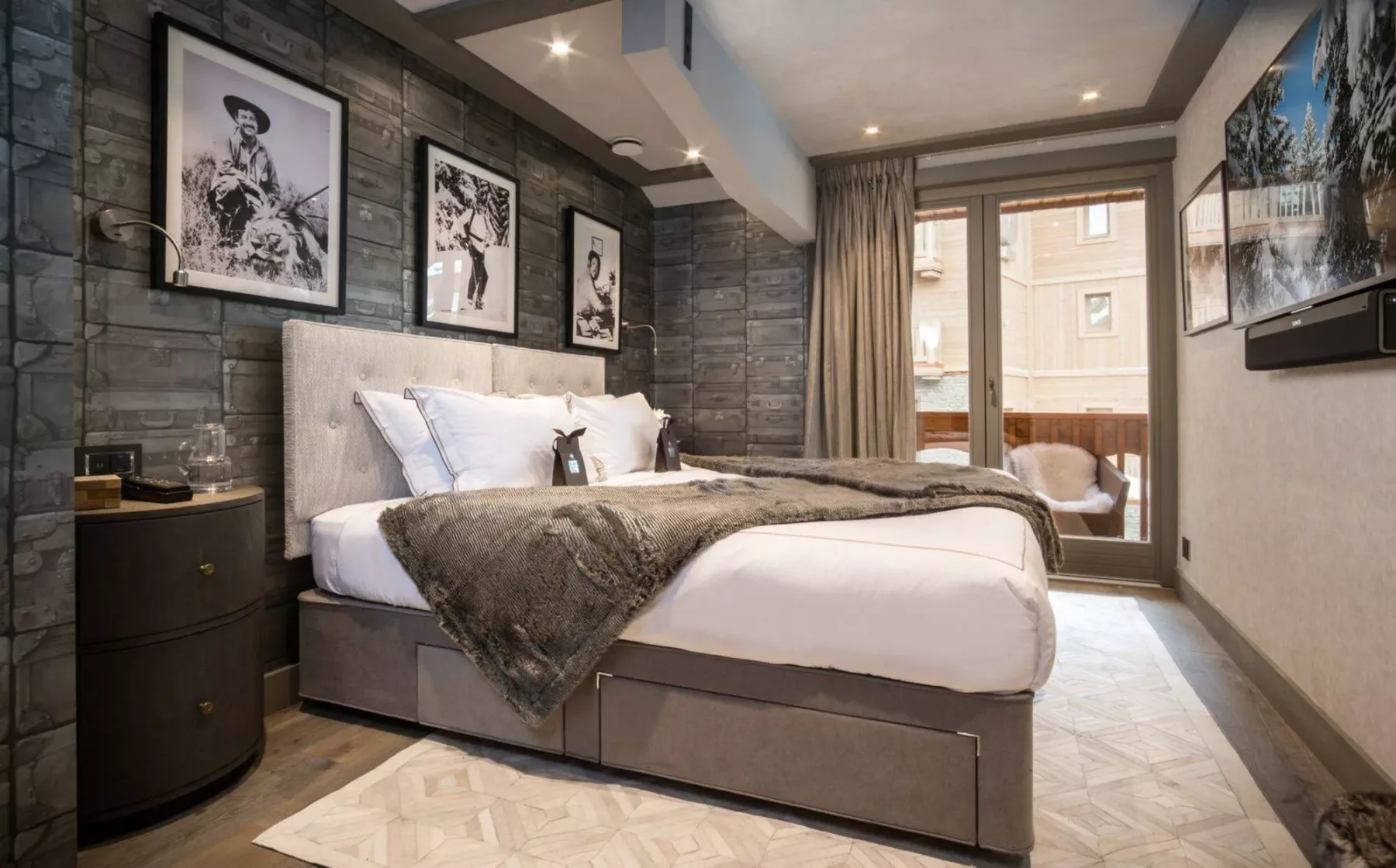 Un dormitorio con una cama grande, cuadros enmarcados y una puerta de cristal hacia un balcón.