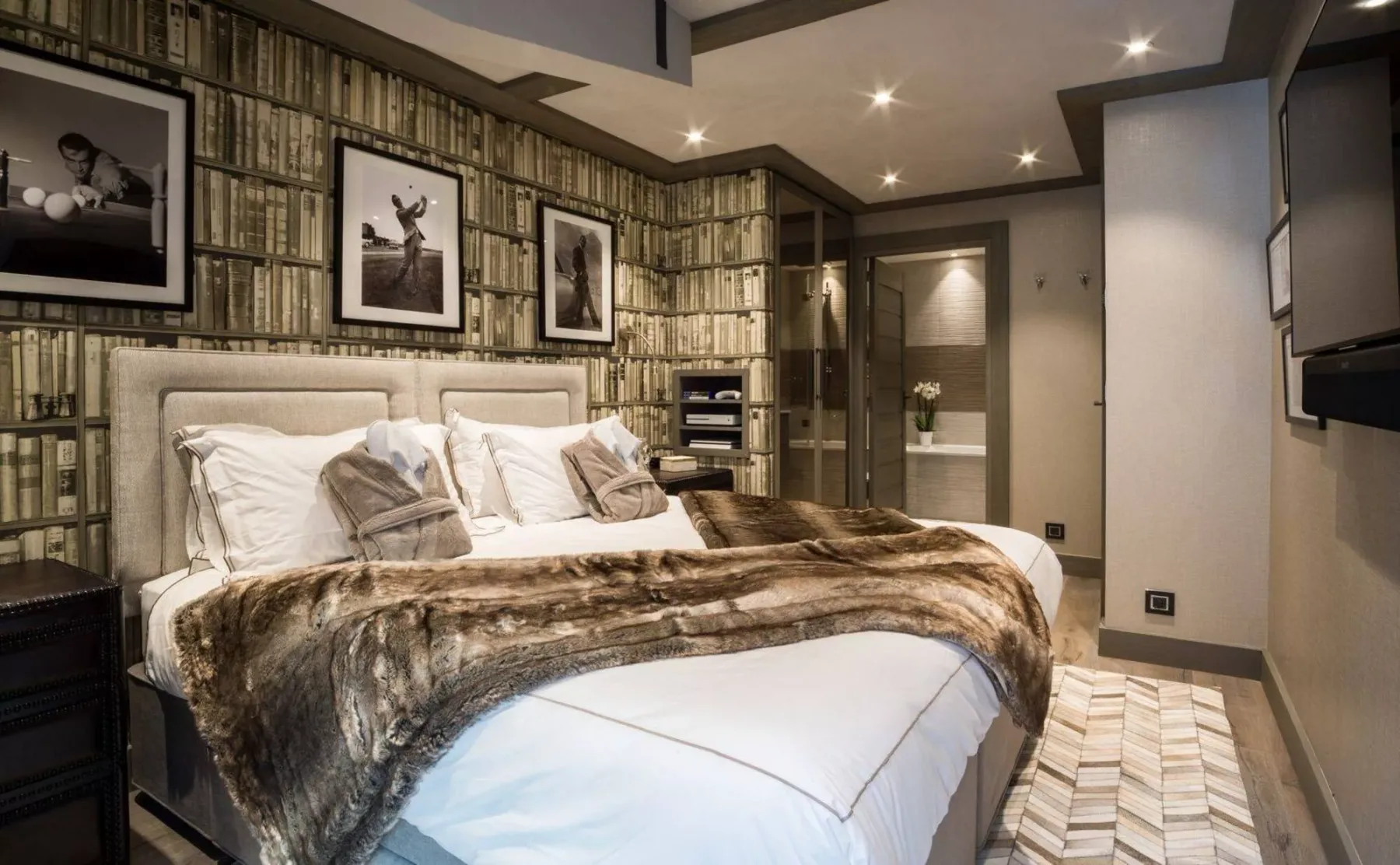 Un dormitorio con una cama grande, papel tapiz estampado y cuadros enmarcados.