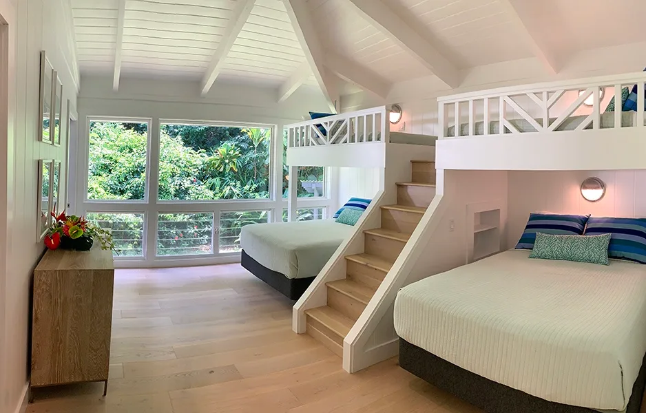 Un dormitorio luminoso con dos camas elevadas, escaleras de madera y grandes ventanas.