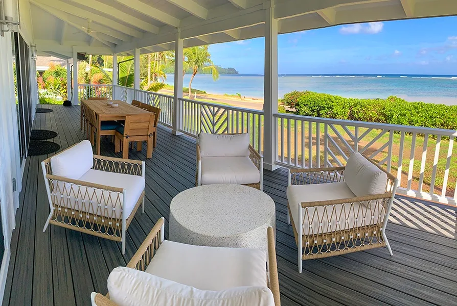 A covered seaside deck has a dining table and seating overlooking the beach.