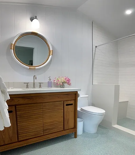 Un baño luminoso con mueble de madera, espejo redondo y ducha.