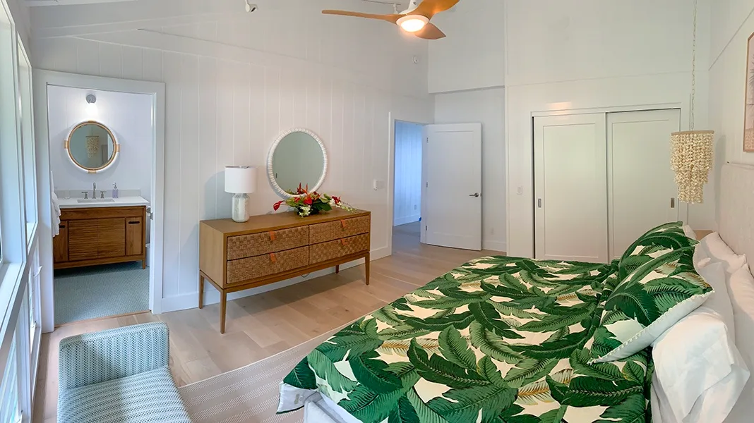 Un dormitorio con una colcha verde estampada de hojas y una cómoda de madera.