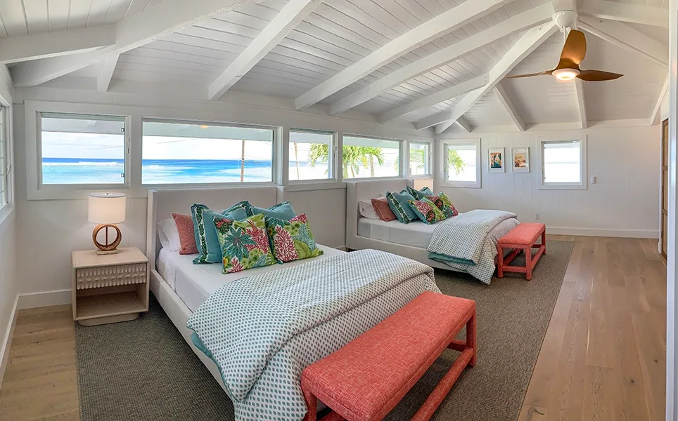 Un dormitorio luminoso con dos camas, cojines coloridos y ventanas con vistas al agua.