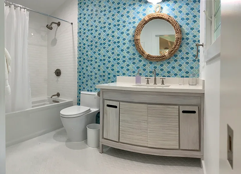 Un baño con bañera, inodoro y tocador bajo un espejo redondo.