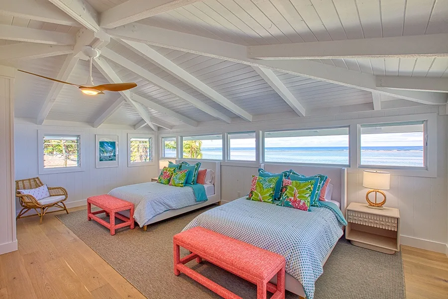 Un dormitorio luminoso con dos camas, cojines coloridos y amplias ventanas con vistas al agua.