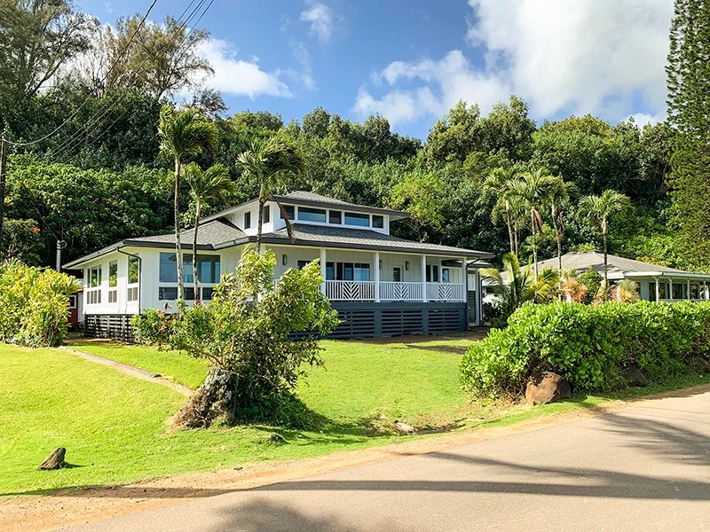 A white house with a covered porch sits among tropical greenery.
