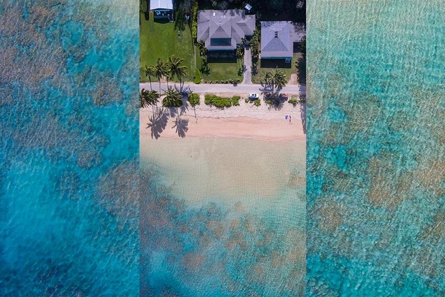 Una vista aérea muestra edificios junto a una playa de arena y aguas turquesas.