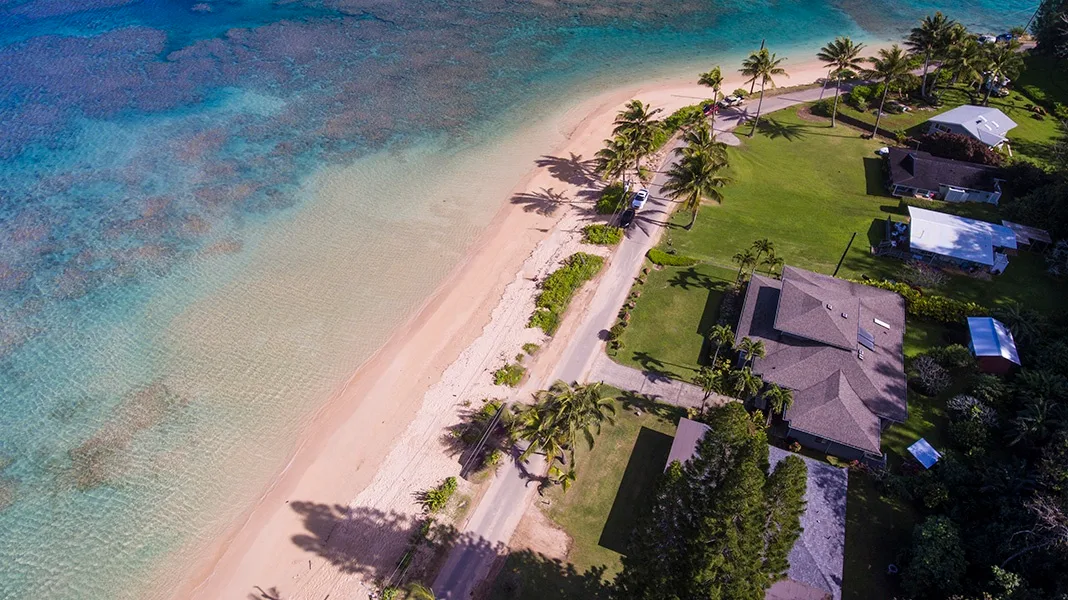 Aerial view of a tropical shoreline with a sandy beach, palm trees, and nearby homes.