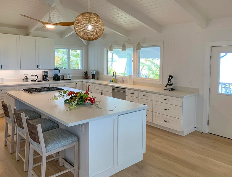 Una cocina luminosa con una isla grande, gabinetes blancos y ventanas.