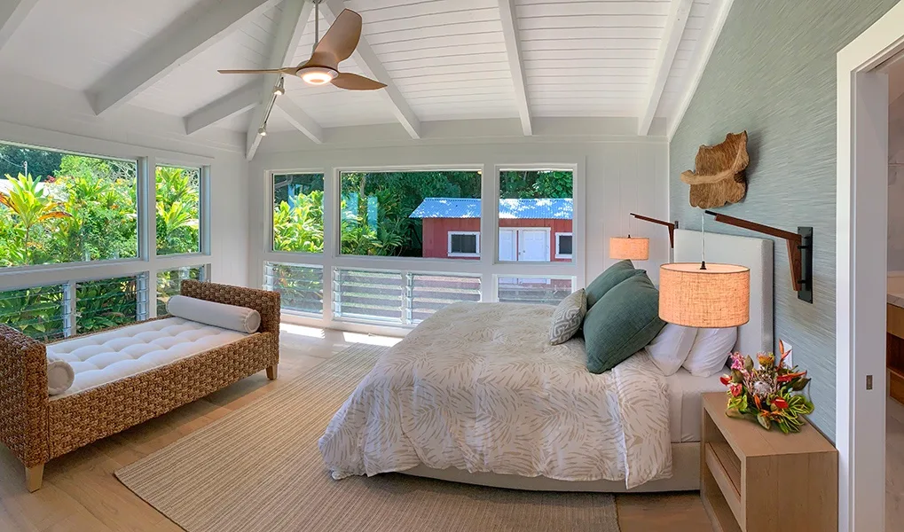 Un dormitorio luminoso con una cama grande y un banco tejido junto a las ventanas.