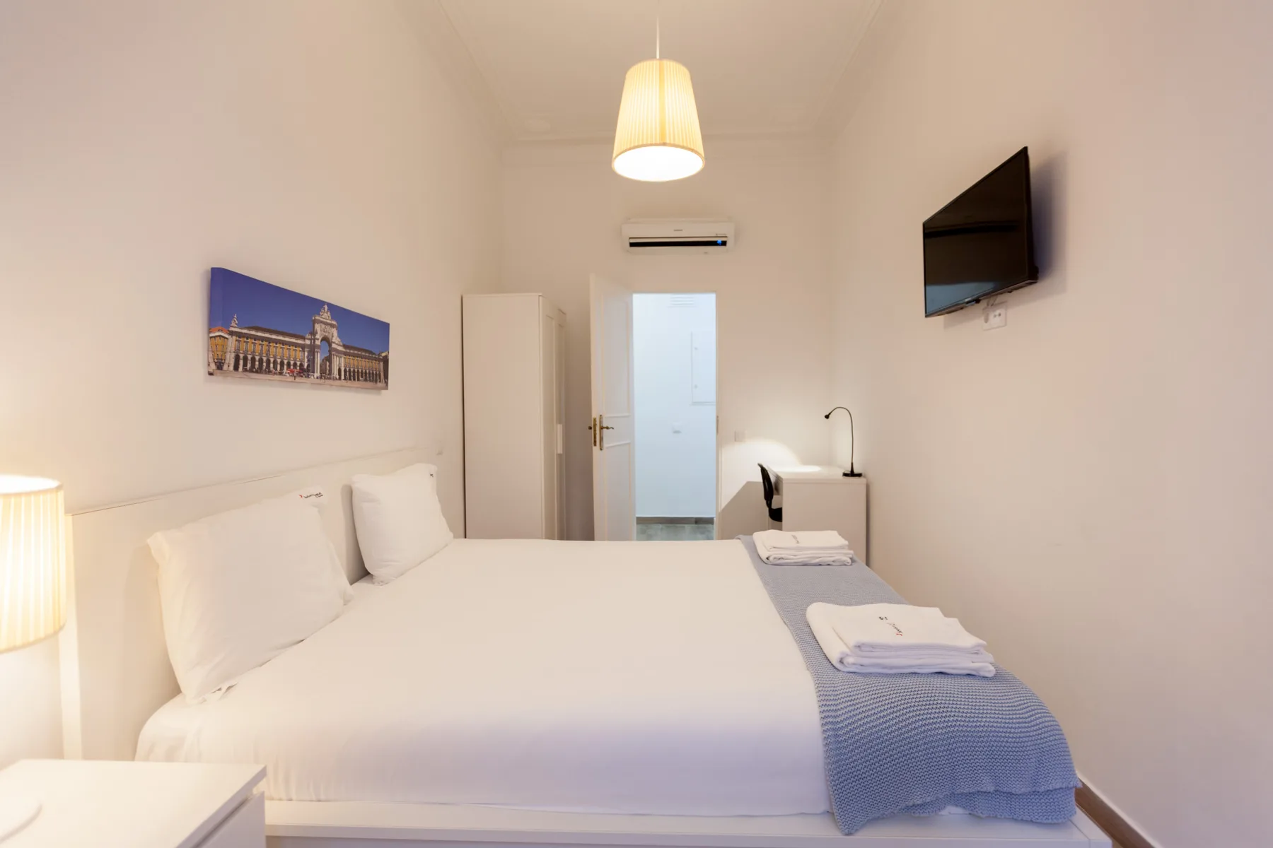 A bedroom with a neatly made bed and a wall-mounted television.