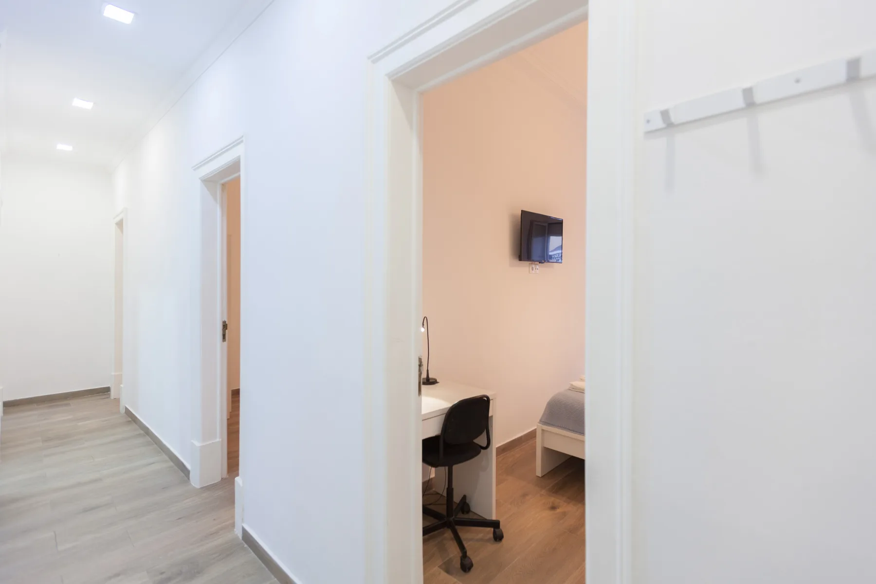 A bright hallway opens onto a bedroom with a desk and seating.