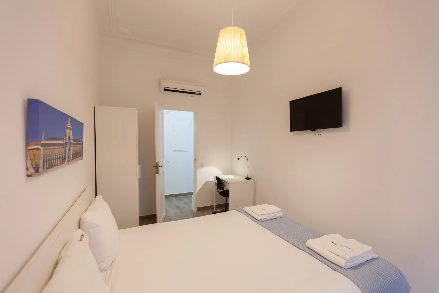 A bedroom with a bed, a wall-mounted television, and a desk beside the doorway.