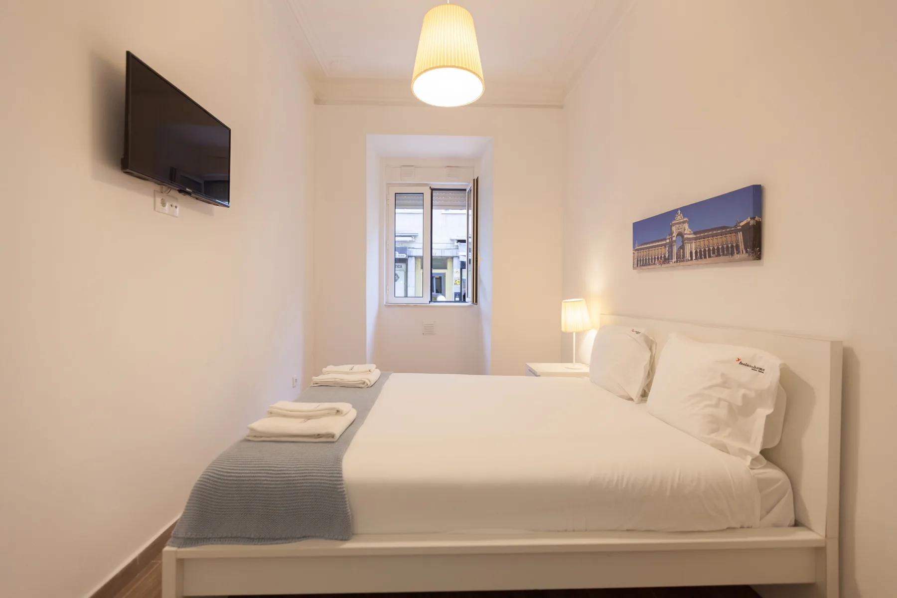 A bedroom with a neatly made bed and a window at the far end.