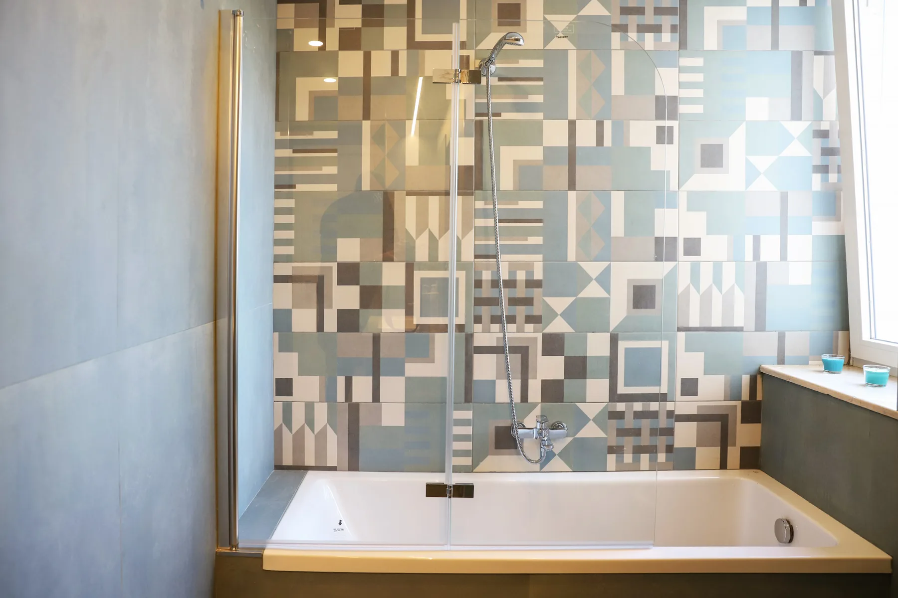 A bathroom with a bathtub and shower against a geometric tiled wall.
