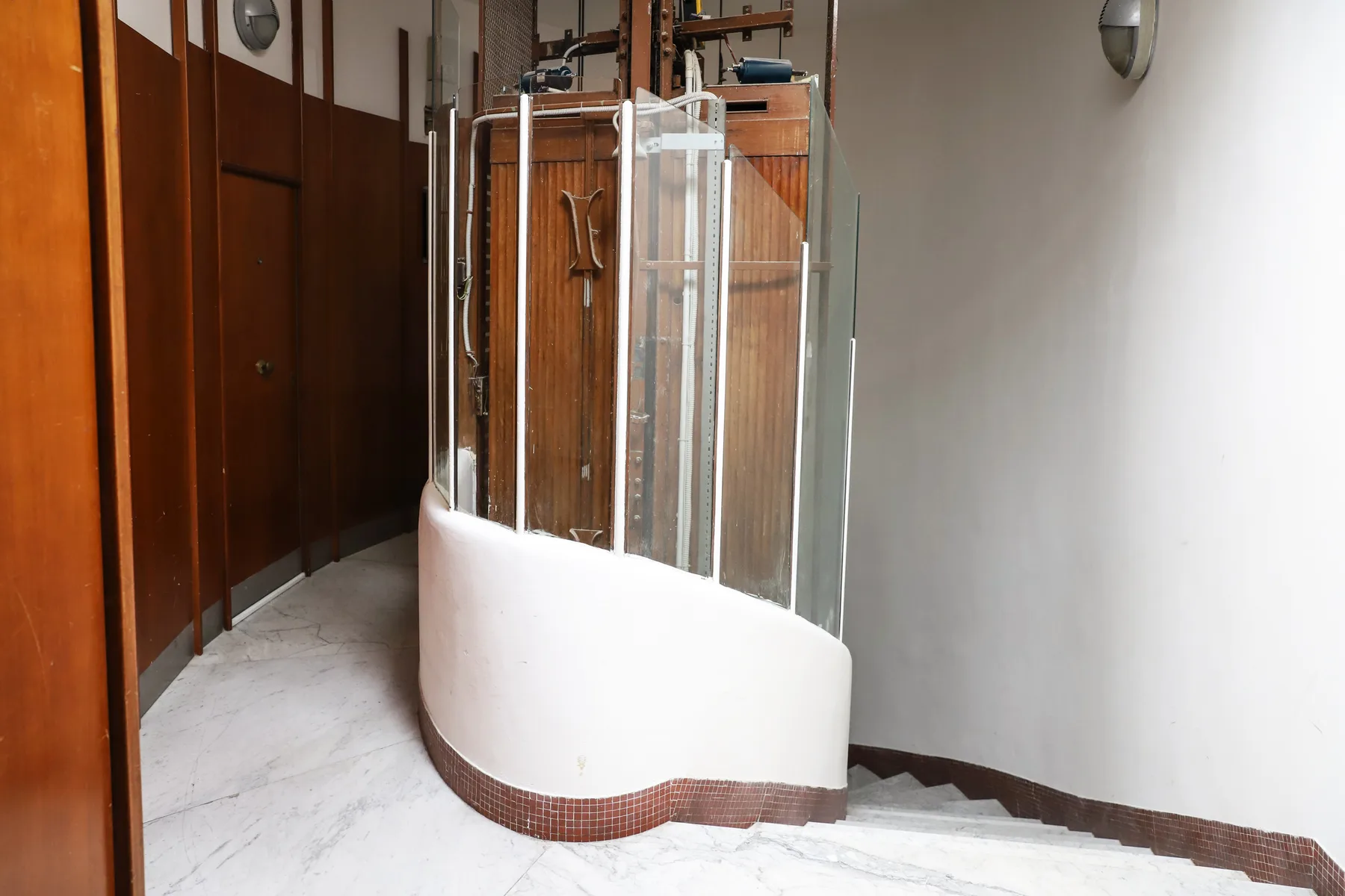 A curved shower enclosure stands beside a staircase in a tiled interior.