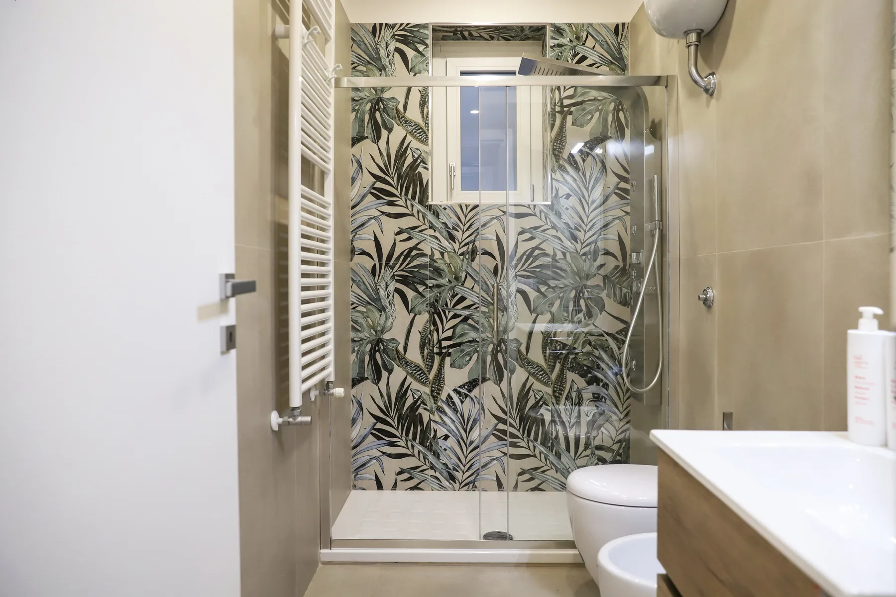 A bathroom with a glass shower and leafy patterned wall tiles.