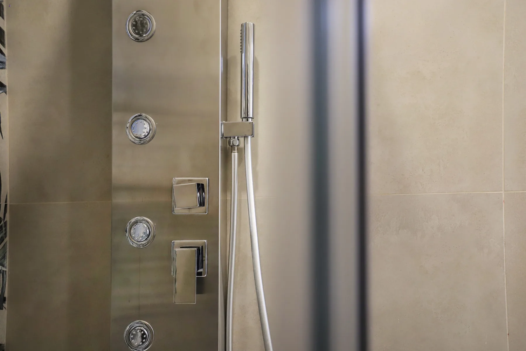 A tiled shower wall with a handheld showerhead and metal controls.