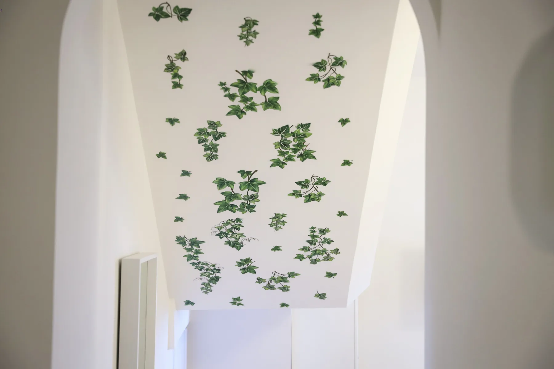 A bright indoor passage has a high curved ceiling decorated with green leaves.