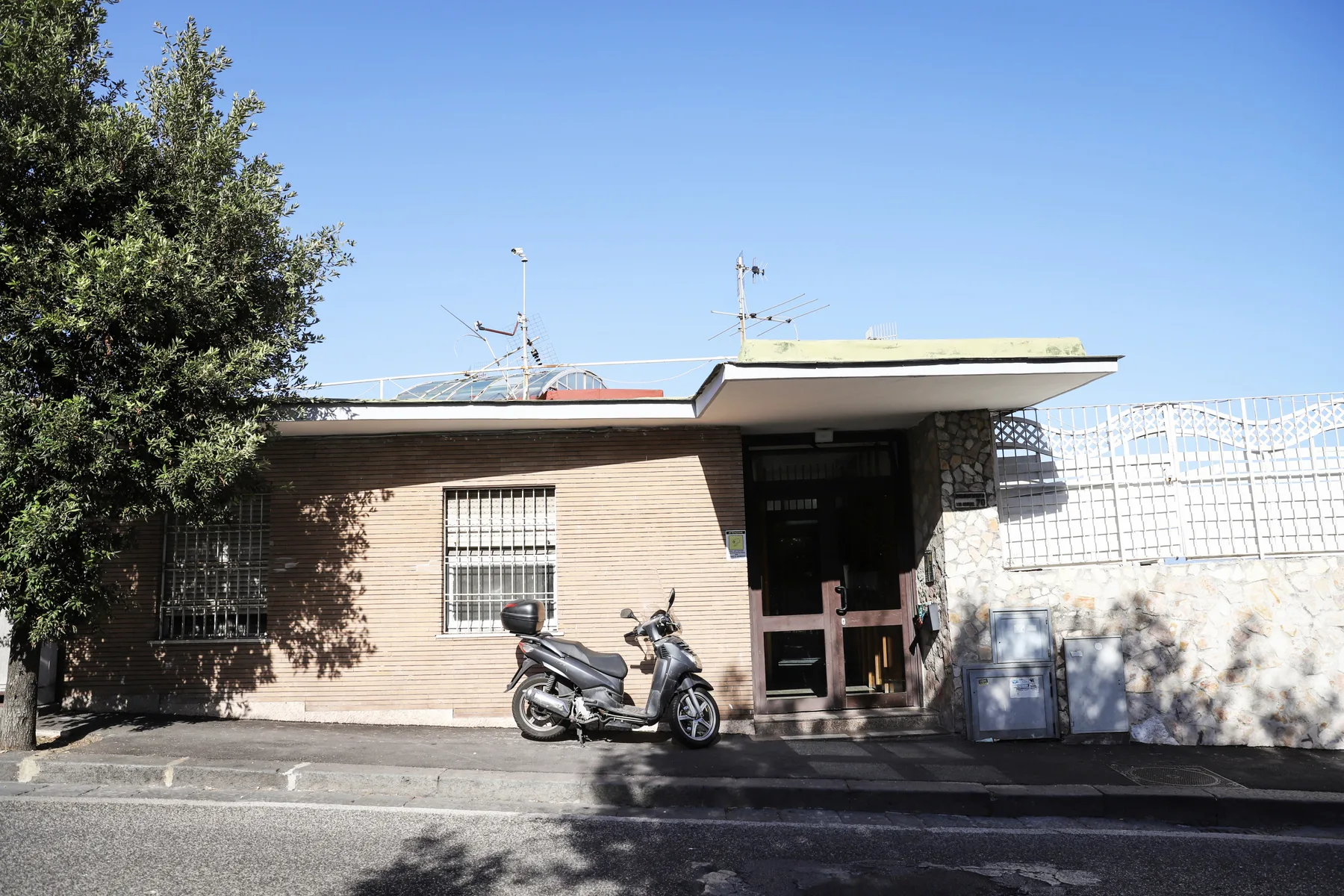 A low brick building with a dark entrance and a scooter parked outside.