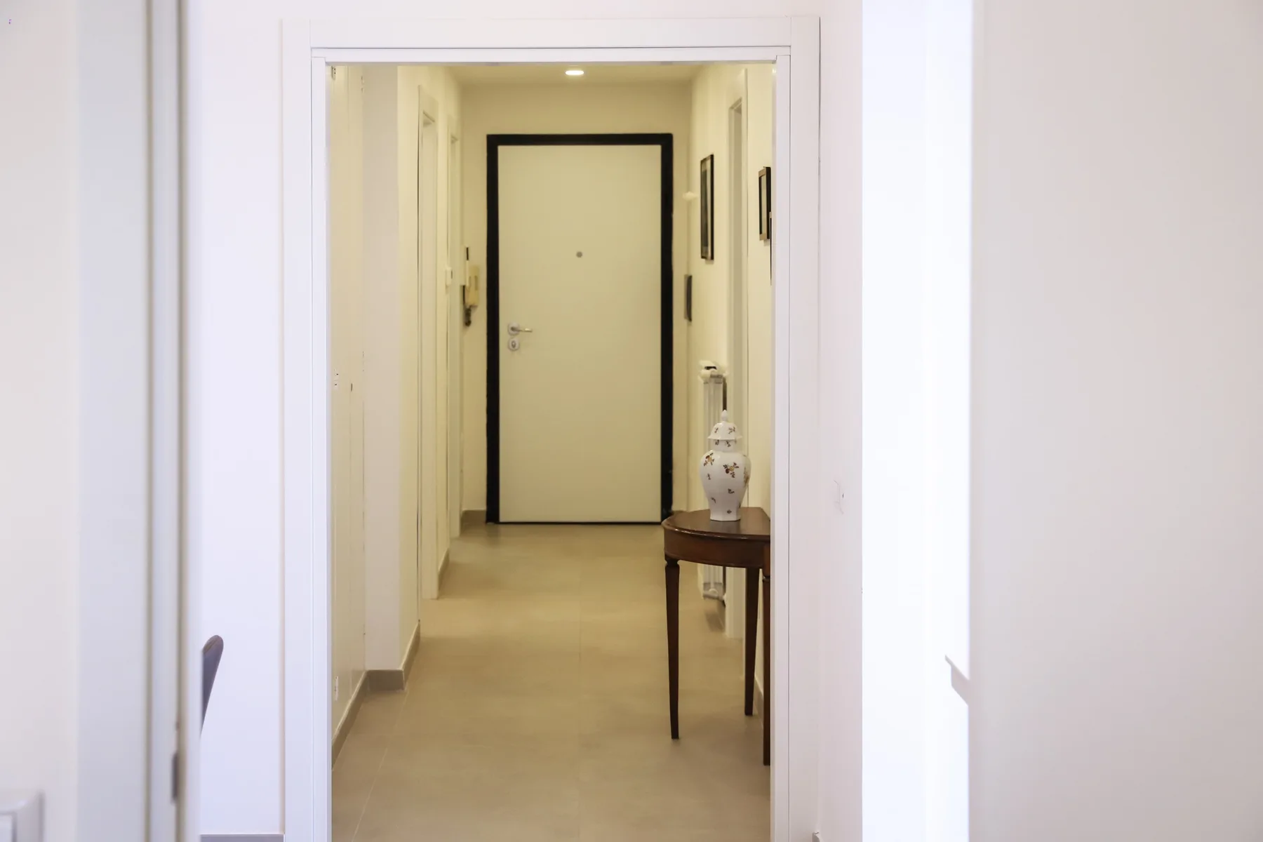 A bright hallway leads to a closed door, with a small table along the wall.