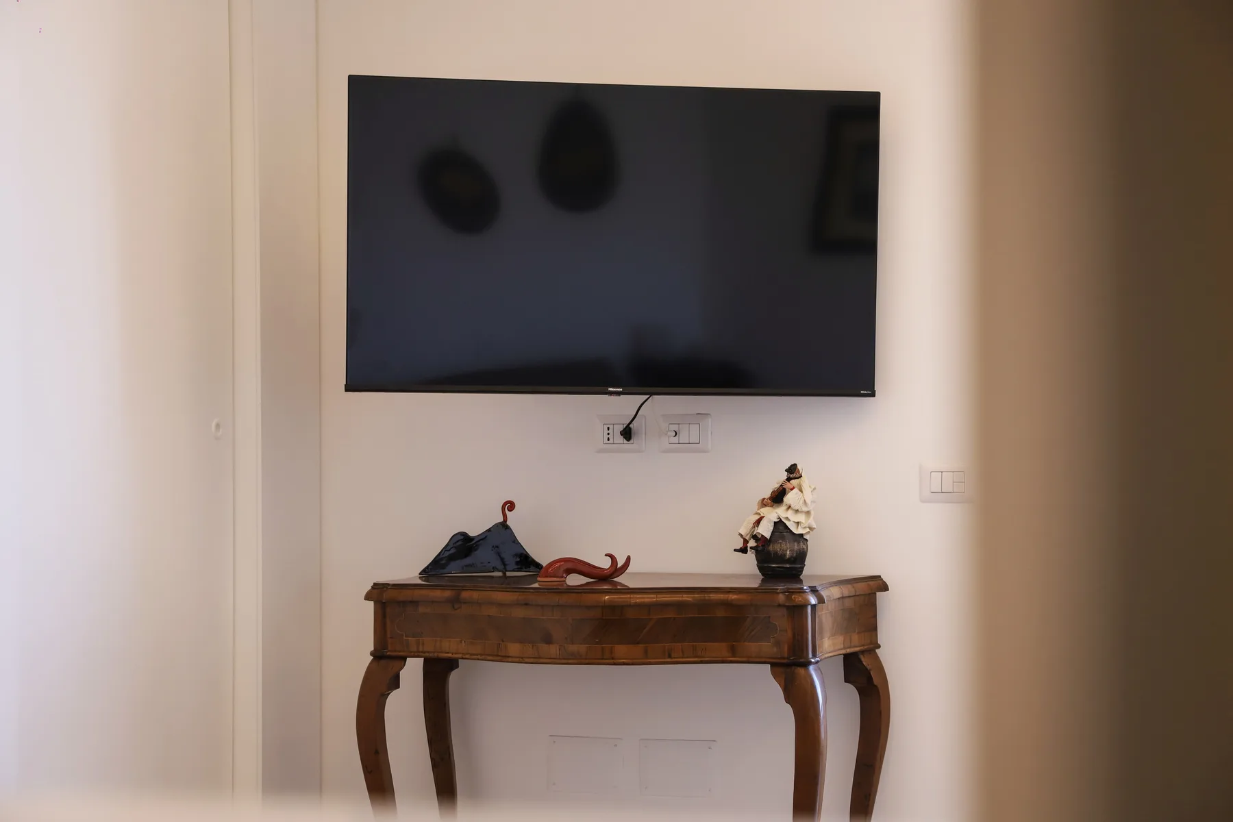A wall-mounted television hangs above a wooden console table with decorative objects.