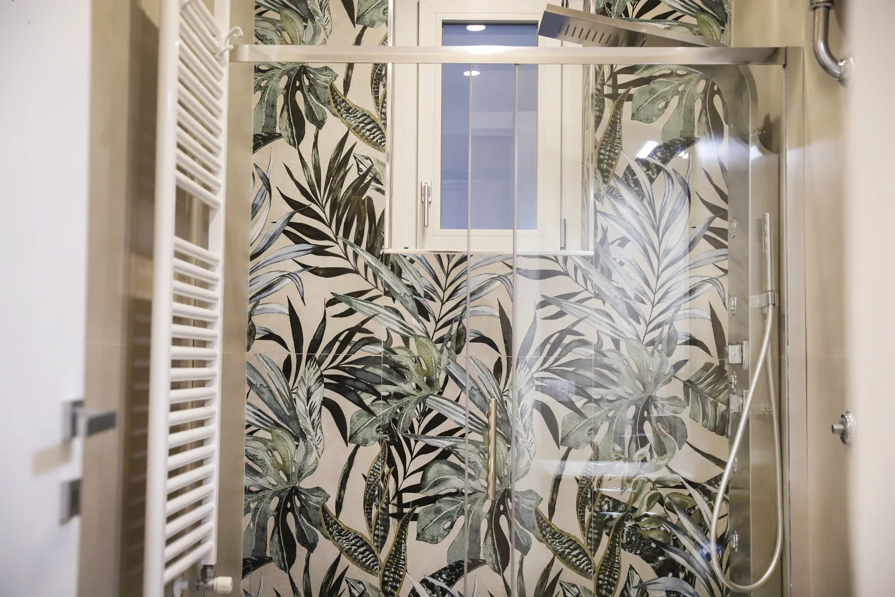 A bathroom shower with leafy patterned wall tiles and a small window.