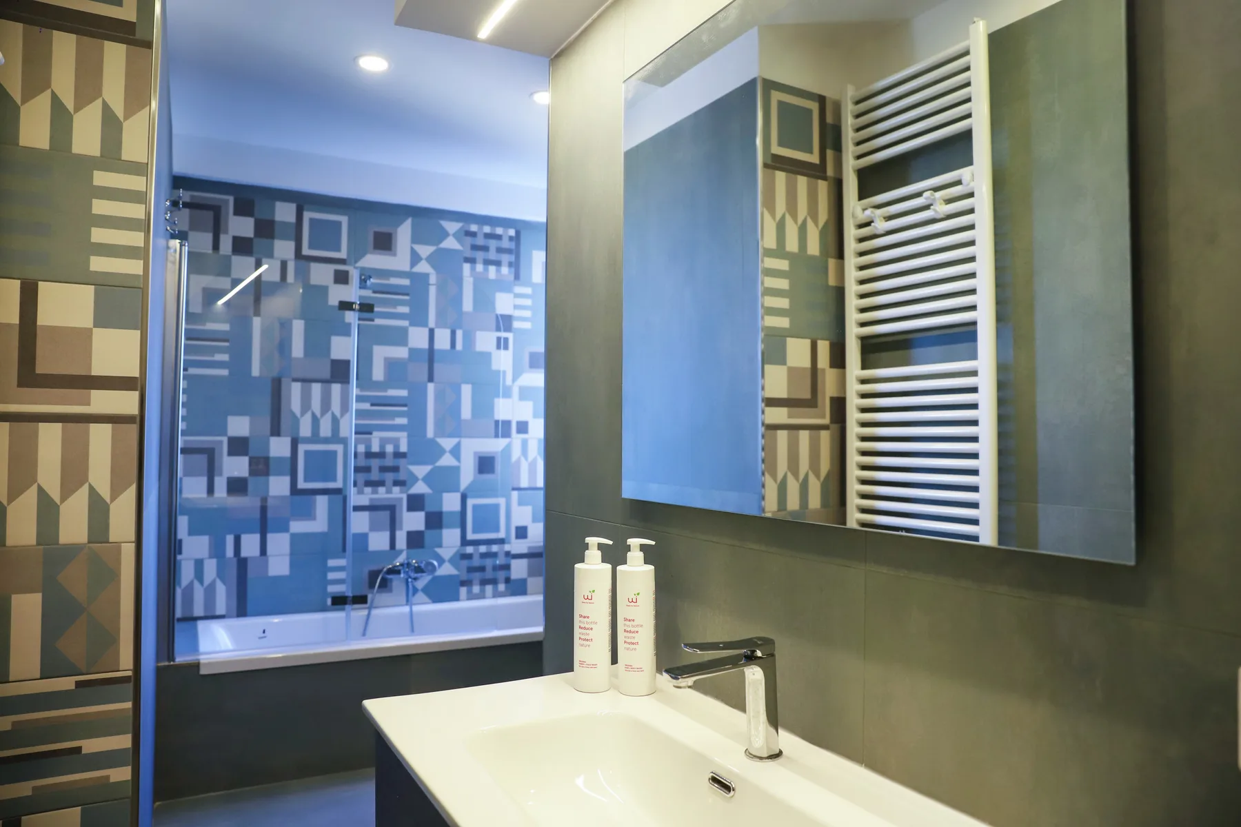 A bathroom with a sink, mirror, and patterned wall tiles.
