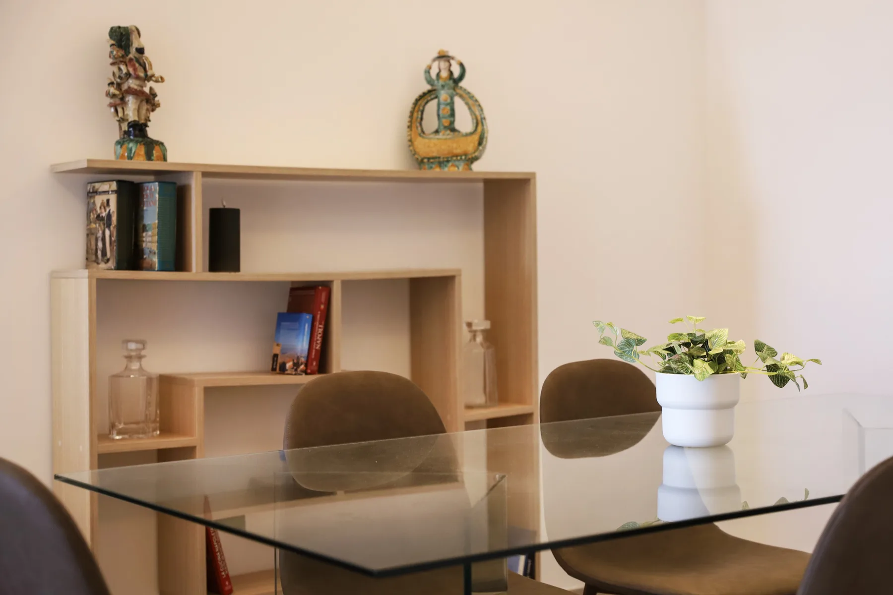 A dining area with a glass table, chairs, and a shelving unit.