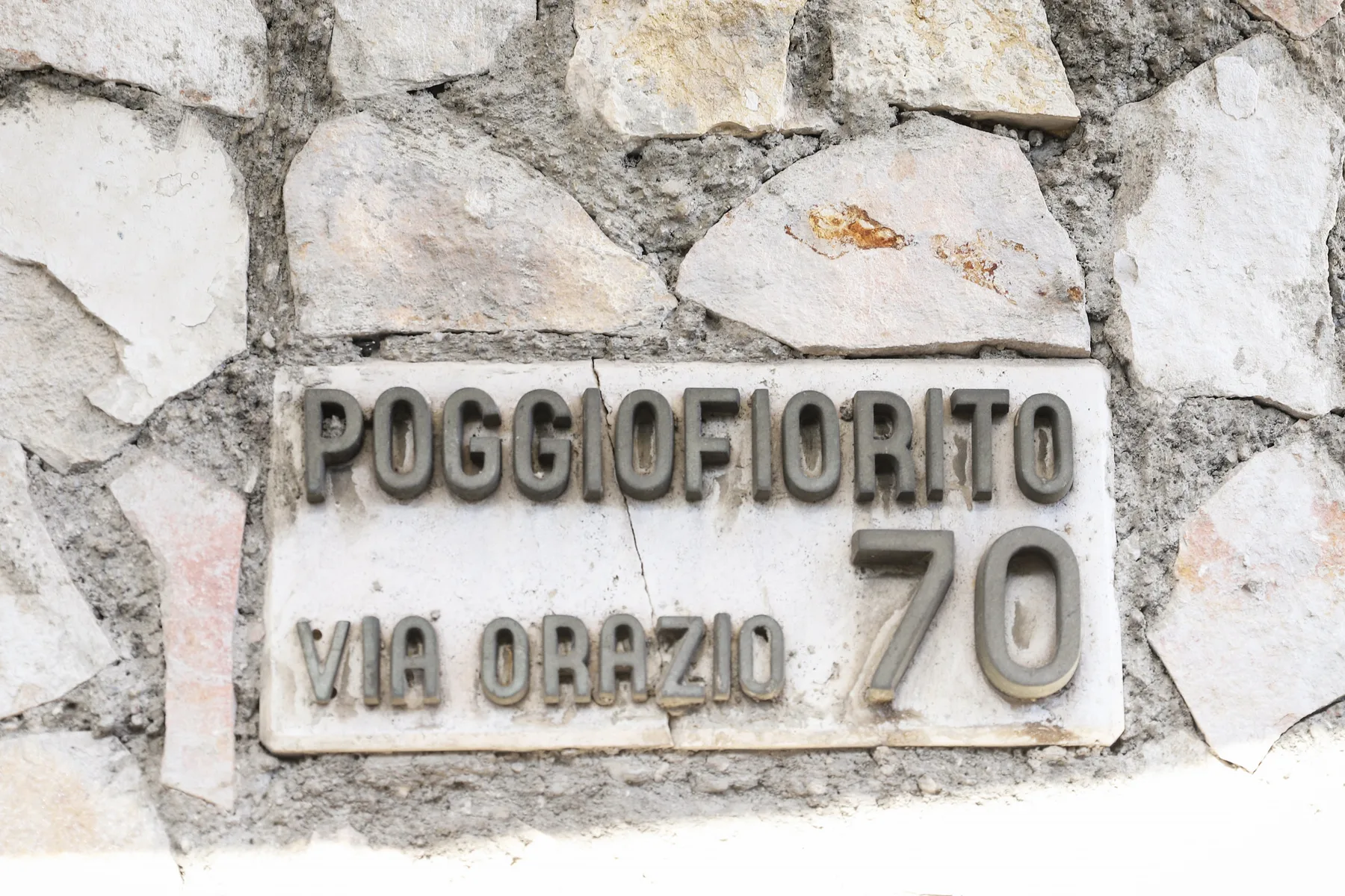 A street name plaque is mounted on a rough stone wall.