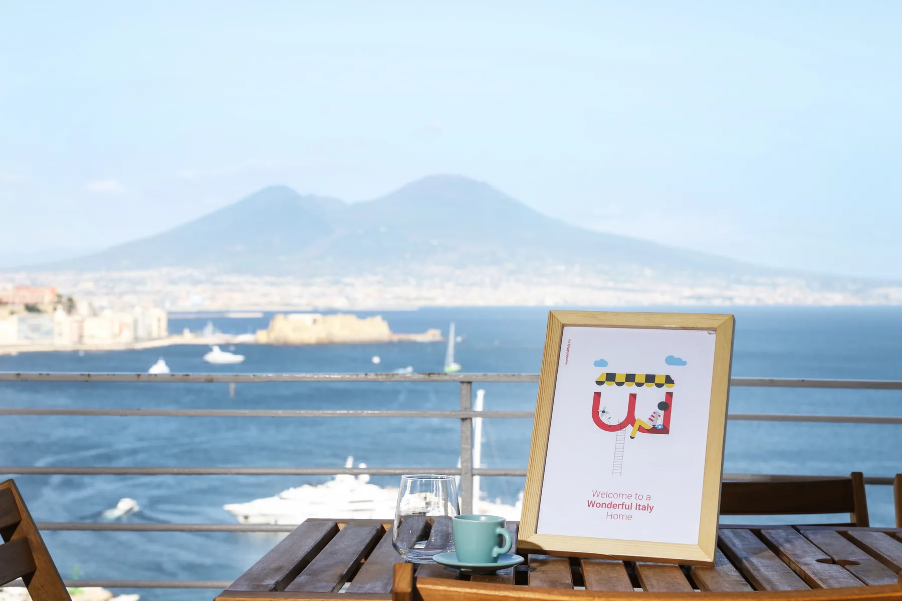 A waterfront terrace table overlooks boats and a distant mountain across the bay.