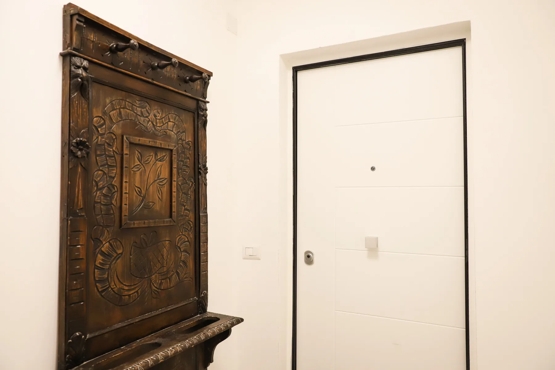An entryway with a white door beside a dark carved wooden wall panel.