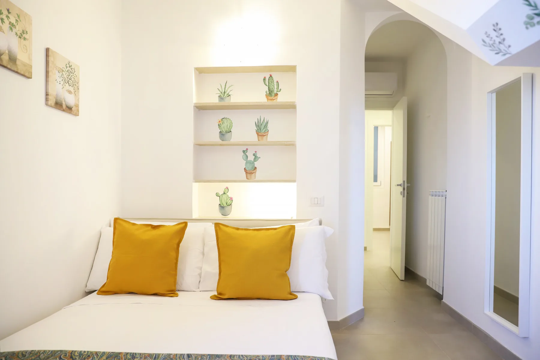 A bright bedroom with a bed beneath shelves displaying small potted plants.