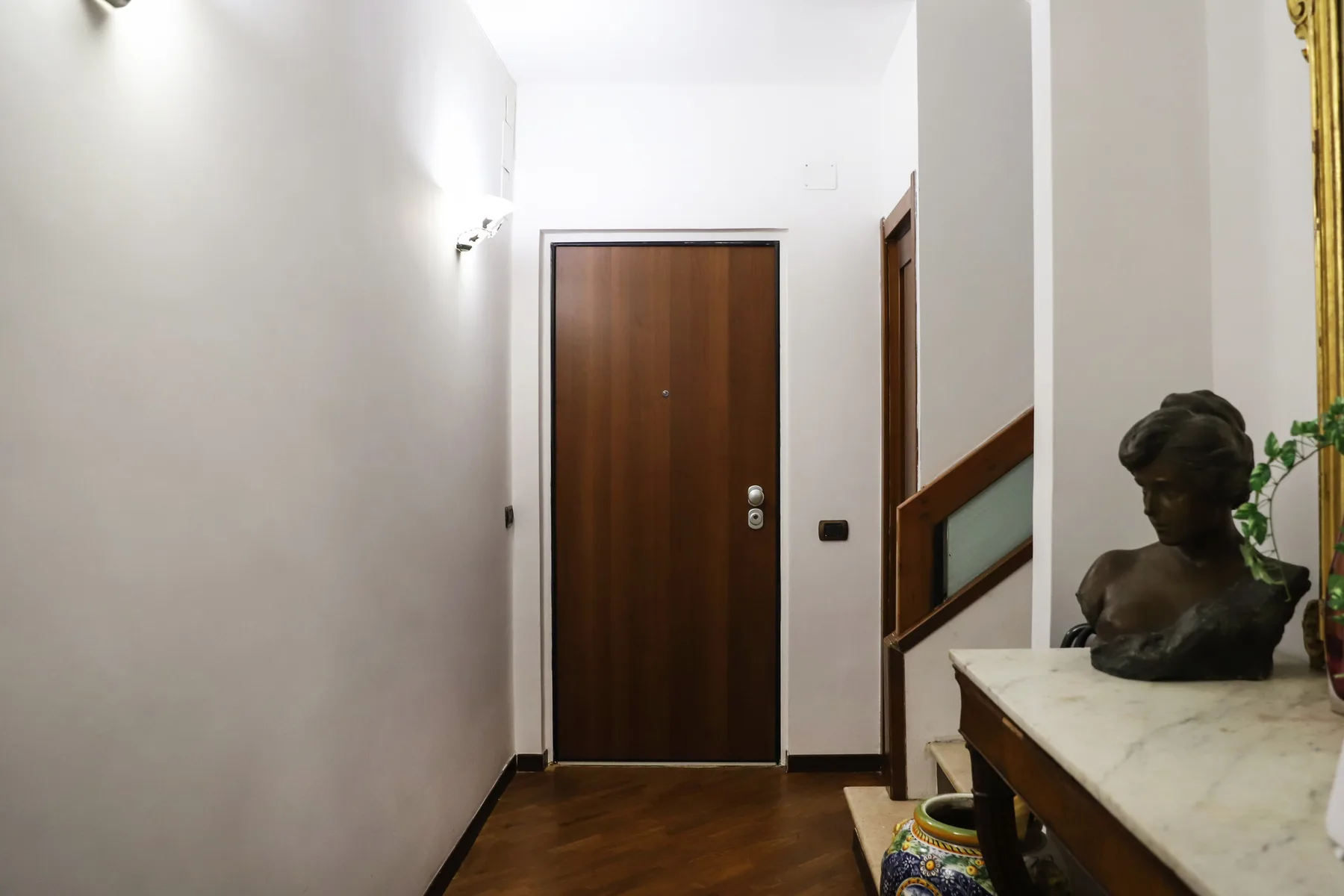 A hallway with a wooden entrance door and a staircase along the wall.
