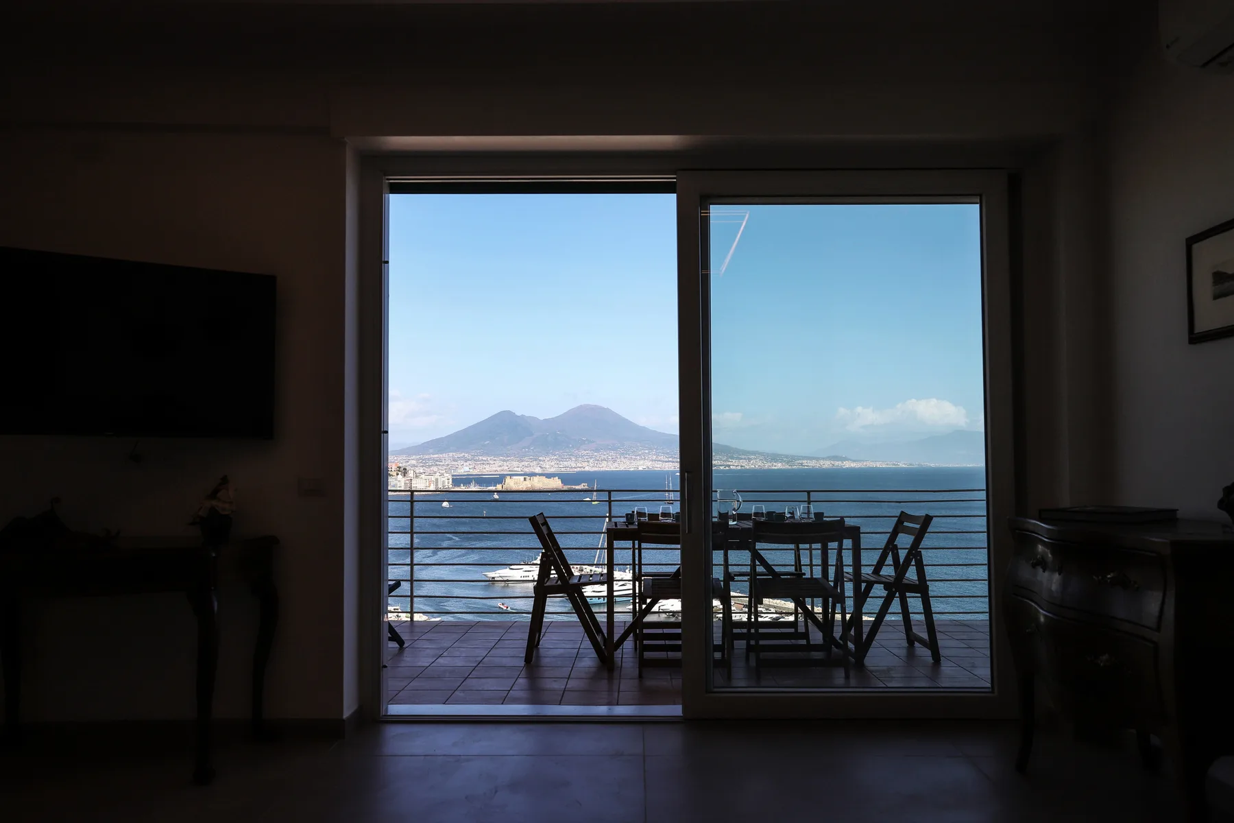 A dining area opens onto a balcony overlooking the sea and distant mountains.