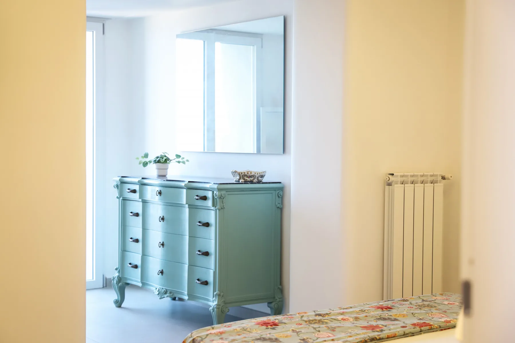A bedroom with a dresser, mirror, and radiator.