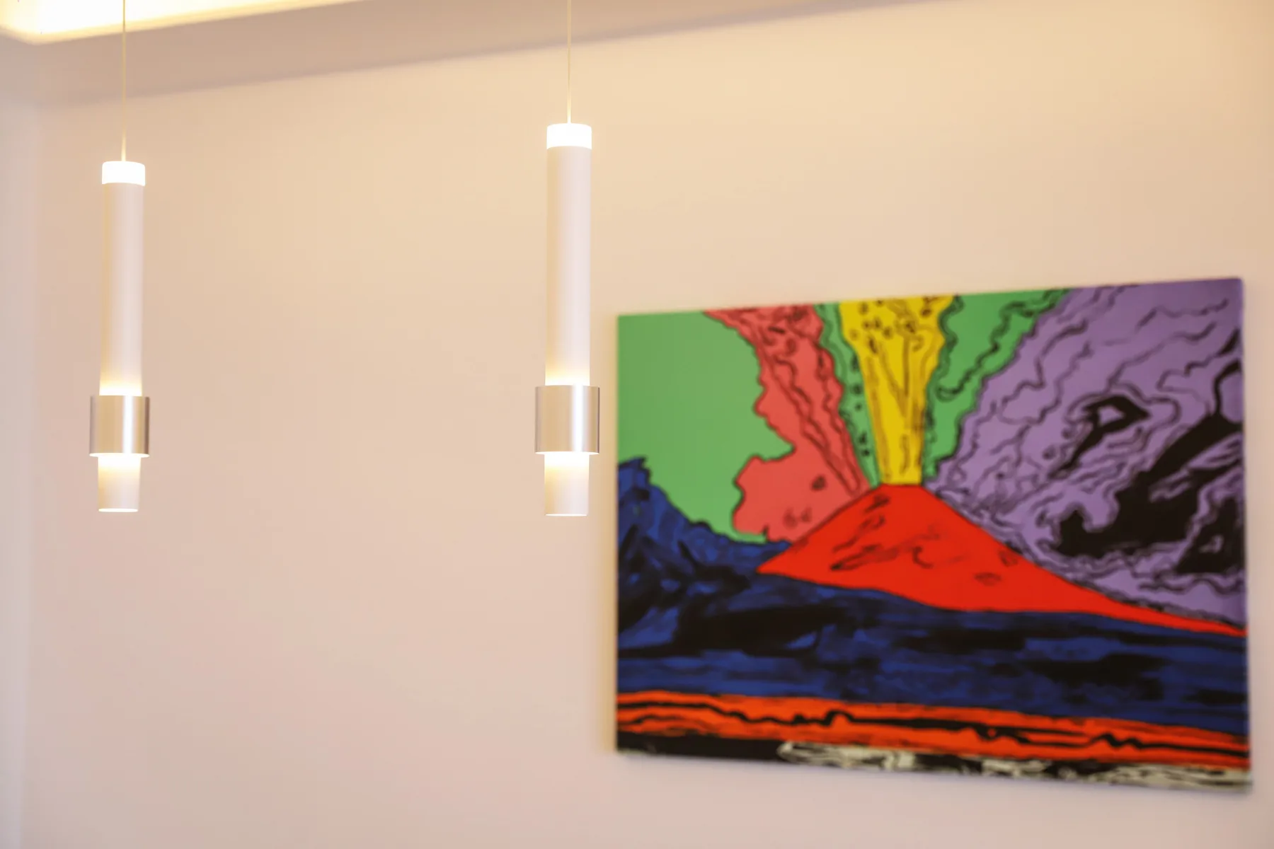 A colorful abstract painting hangs on a pale wall beneath two pendant lights.