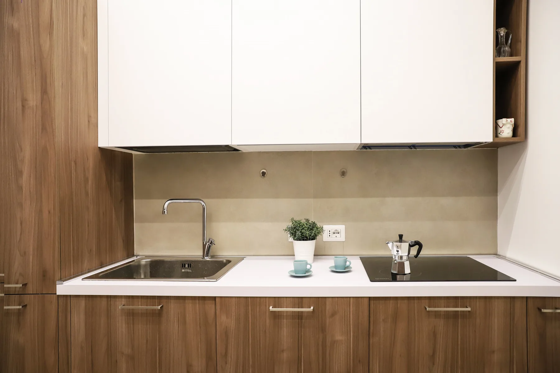 A modern kitchen counter with a sink, stovetop, and white cabinets.