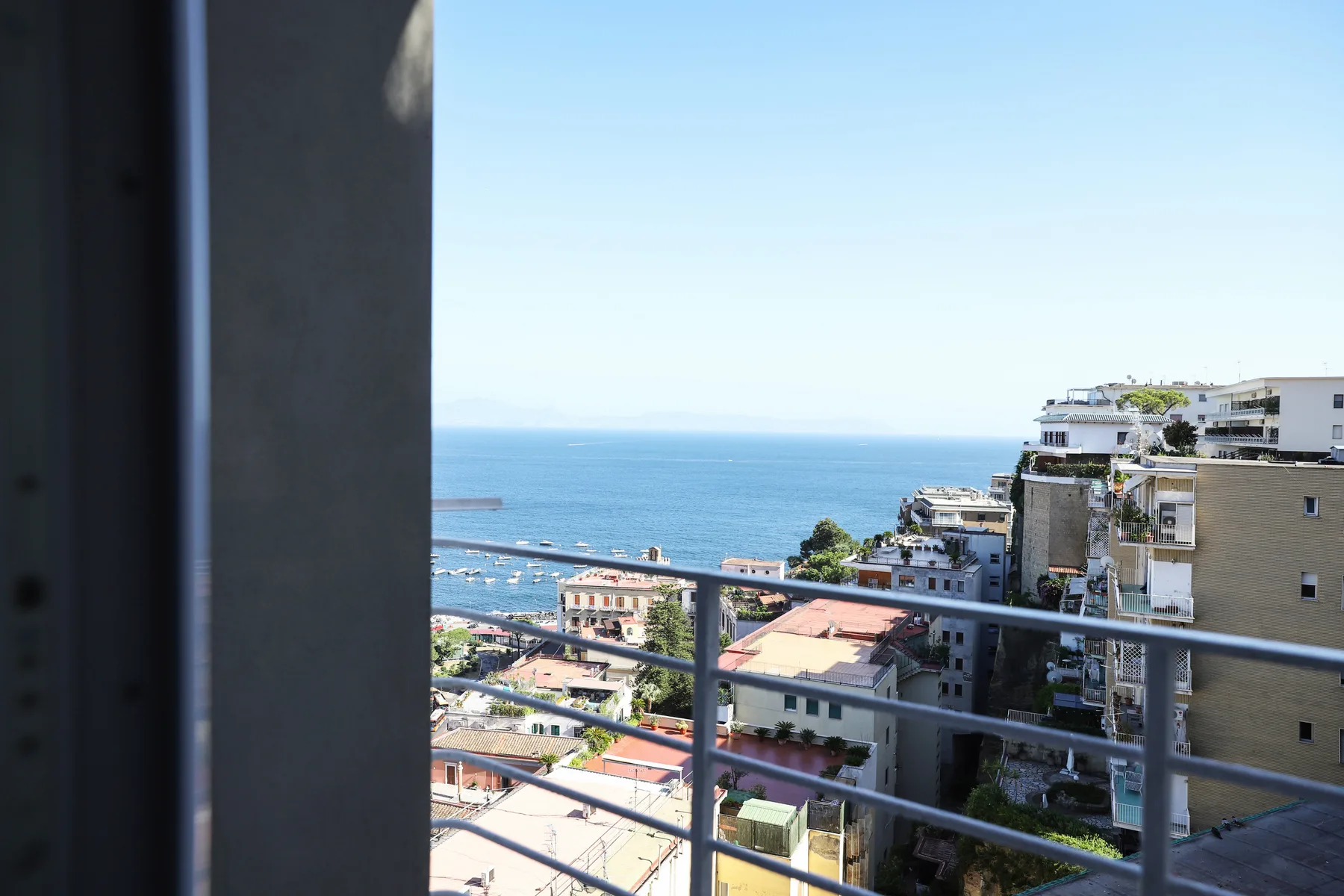 A balcony overlooks the sea and a cluster of coastal buildings.