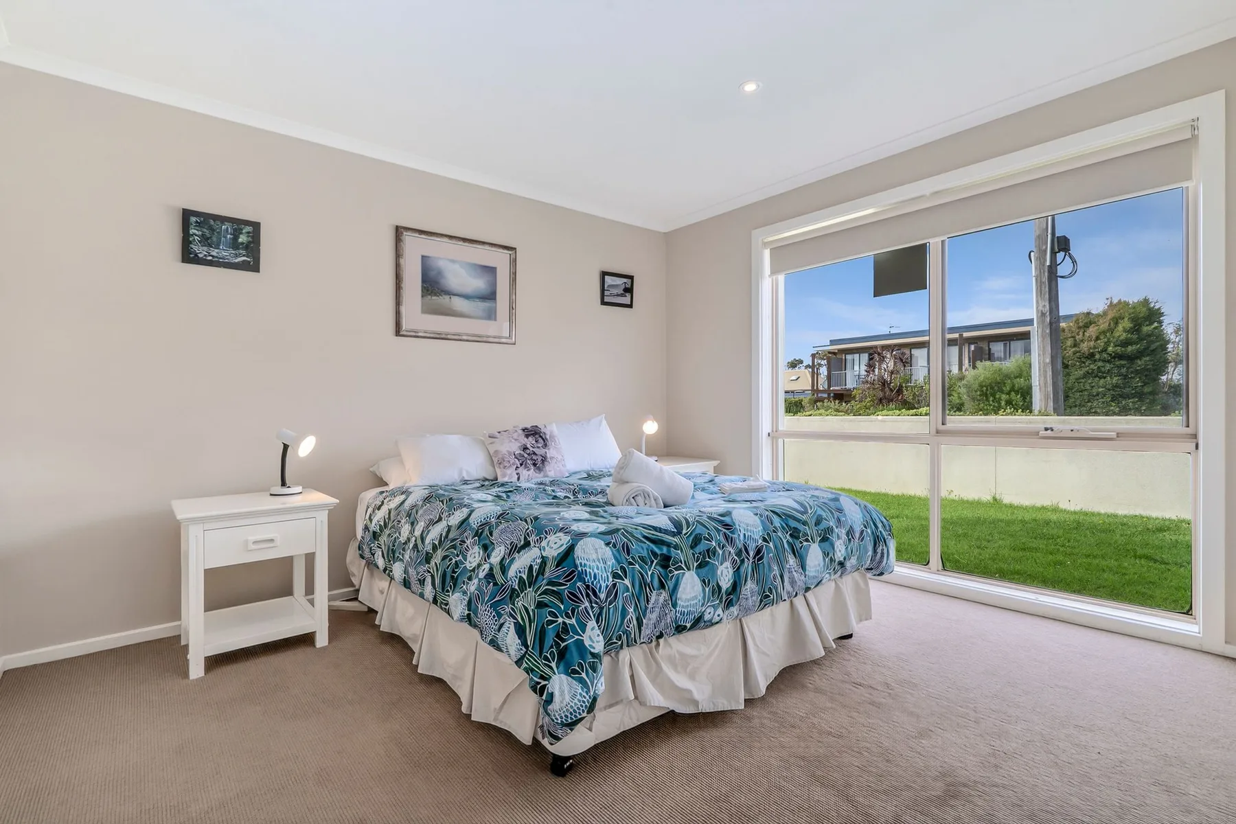 Un dormitorio con una cama junto a una ventana grande que da a un patio con césped.