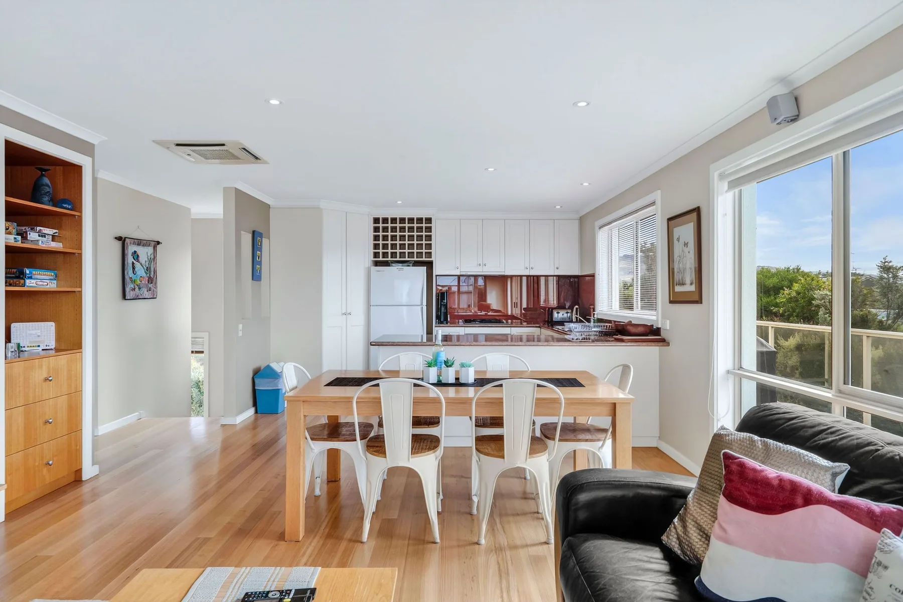 Una luminosa zona abierta de comedor y cocina con una mesa junto a grandes ventanas.
